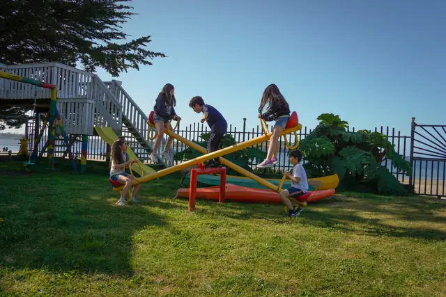 Niños en el balancín múltiple del jardín, con el mar de Playa Lechagua detrás