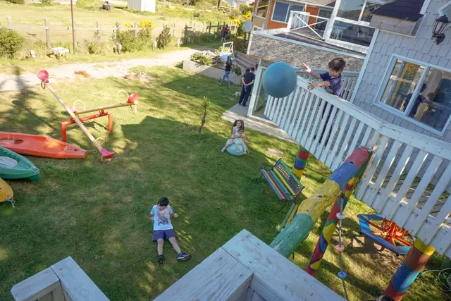 Zona de juegos de Cabañas Kompatzki: pasto, juegos de colores, kayaks y las cabañas al fondo, en Playa Lechagua