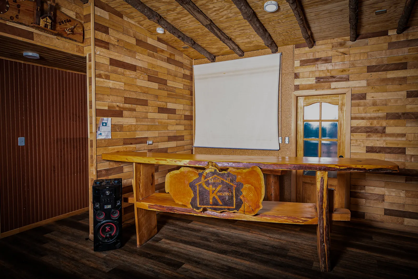 Barra de madera con el logo tallado de Kompatzki y telón de proyección en el salón de eventos