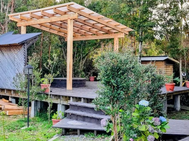 Pérgola de madera y deck del sector de la tinaja, de día, con el jardín alrededor